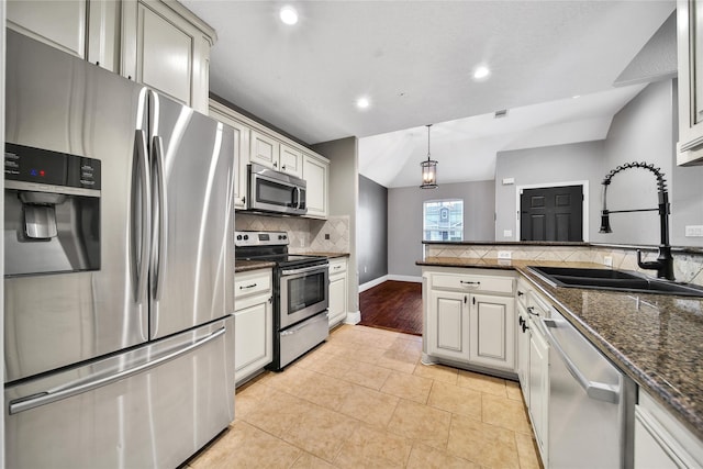 kitchen featuring appliances with stainless steel finishes, a sink, a peninsula, tasteful backsplash, and hanging light fixtures