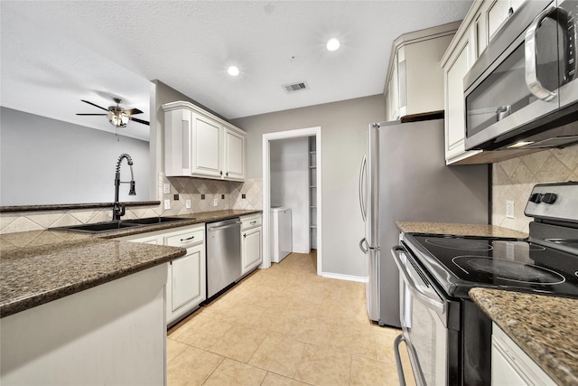 kitchen with appliances with stainless steel finishes, a sink, backsplash, a ceiling fan, and washer / clothes dryer