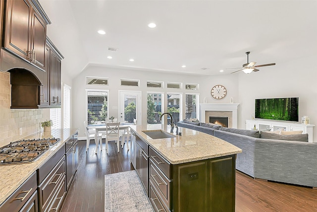 16819 Big Reed Dr, Humble, TX 77346 - kitchen featuring a sink, a warm lit fireplace, stainless steel gas stovetop, ceiling fan, and tasteful backsplash