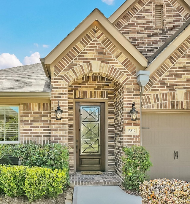 16819 Big Reed Dr, Humble, TX 77346 - view of exterior entry featuring brick siding, roof with shingles, and a garage