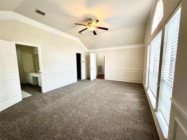 unfurnished bedroom featuring vaulted ceiling, a decorative wall, carpet, wainscoting, and ornamental molding