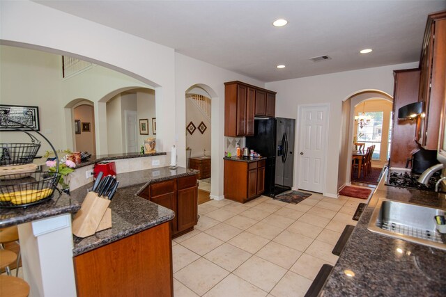 20018 Rene Creek Ct, Spring, TX 77388 - kitchen featuring a sink, black fridge, light tile patterned flooring, arched walkways, and dark stone counters