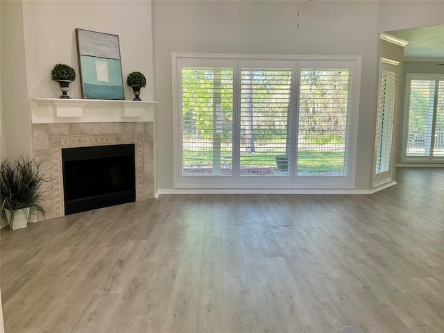 unfurnished living room featuring wood finished floors, ornamental molding, a tile fireplace, and baseboards