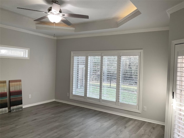 spare room featuring a tray ceiling, ceiling fan, dark wood-style floors, crown molding, and baseboards