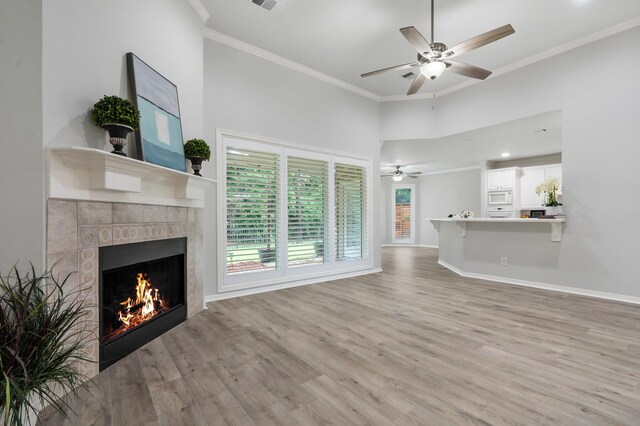 25818 Overlake Dr, Spring, TX 77380 - unfurnished living room featuring a tile fireplace, ornamental molding, a ceiling fan, light wood finished floors, and a towering ceiling