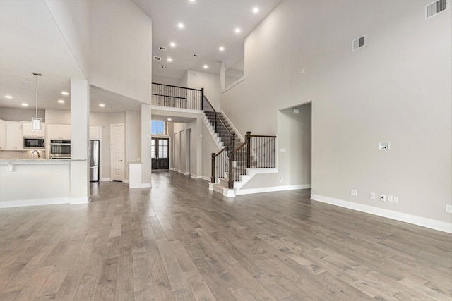 28622 Mountain Timber Ct, Fulshear, TX 77441 - unfurnished living room with light wood-type flooring, stairs, recessed lighting, a towering ceiling, and baseboards