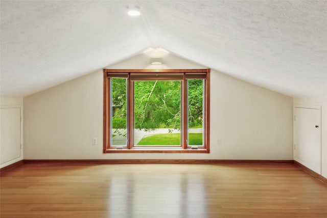 bonus room with wood finished floors, baseboards, vaulted ceiling, and a textured ceiling