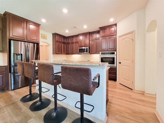 2755 Overlook Rd, Caldwell, TX 77836 - kitchen featuring stainless steel appliances, arched walkways, light wood-style flooring, a kitchen breakfast bar, and tasteful backsplash