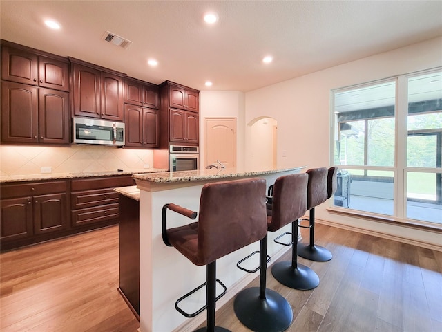 2755 Overlook Rd, Caldwell, TX 77836 - kitchen with stainless steel appliances, a breakfast bar, light wood-type flooring, light stone counters, and decorative backsplash