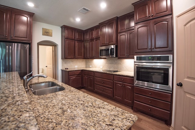 2755 Overlook Rd, Caldwell, TX 77836 - kitchen featuring appliances with stainless steel finishes, a sink, arched walkways, wood finished floors, and tasteful backsplash