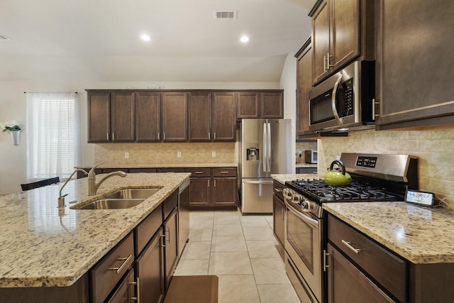 22078 Sun Haven Ln, Porter, TX 77365 - kitchen featuring appliances with stainless steel finishes, a sink, light stone countertops, decorative backsplash, and dark brown cabinetry