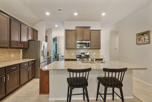 22078 Sun Haven Ln, Porter, TX 77365 - kitchen featuring stainless steel appliances, a center island with sink, light stone countertops, a sink, and light tile patterned floors