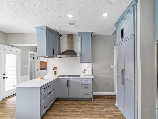 20647 Laurel Lock Dr, Katy, TX 77450 - kitchen featuring wall chimney range hood, a peninsula, a textured ceiling, light wood-type flooring, and gray cabinetry