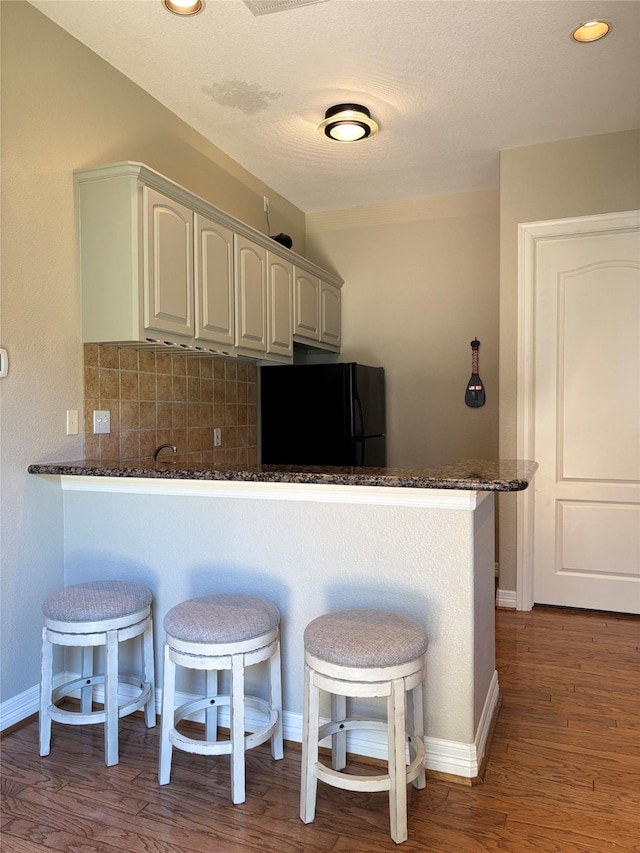 2331 Scottsdale Ct, League City, TX 77573 - kitchen with freestanding refrigerator, a peninsula, backsplash, a breakfast bar, and wood finished floors