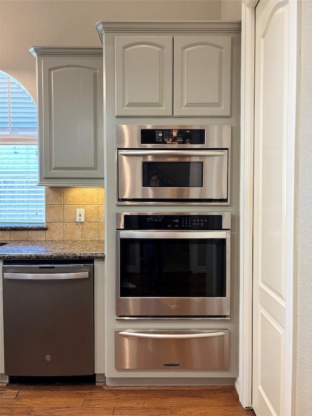 2331 Scottsdale Ct, League City, TX 77573 - kitchen with appliances with stainless steel finishes, a warming drawer, wood finished floors, dark stone counters, and backsplash