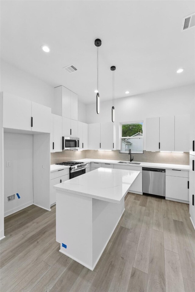 5203 San Juan St, Houston, TX 77020 - kitchen with stainless steel appliances, a sink, light wood finished floors, white cabinetry, and hanging light fixtures