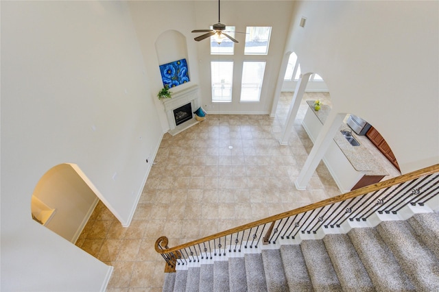 28015 Heritage Stream Dr, Katy, TX 77494 - stairs featuring ceiling fan, arched walkways, a fireplace, baseboards, and a high ceiling