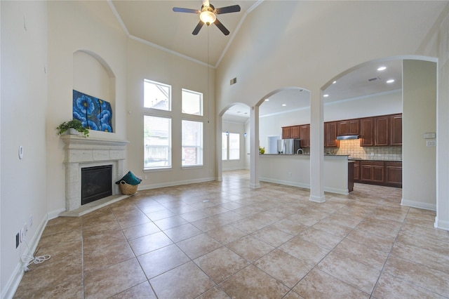 28015 Heritage Stream Dr, Katy, TX 77494 - unfurnished living room with a ceiling fan, a towering ceiling, a fireplace with raised hearth, ornamental molding, and light tile patterned floors