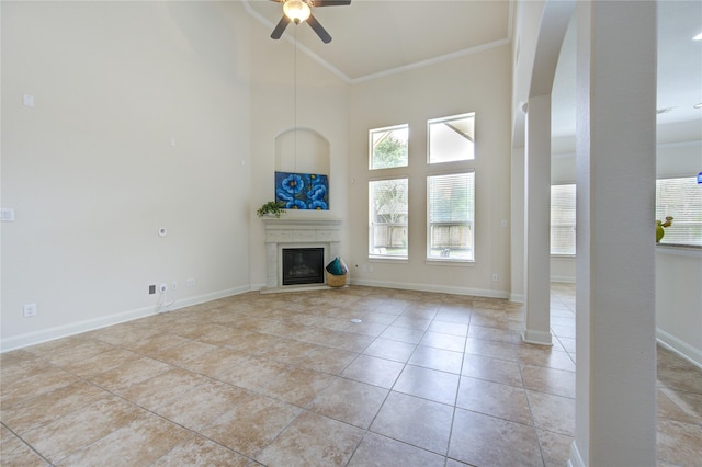 28015 Heritage Stream Dr, Katy, TX 77494 - unfurnished living room featuring a ceiling fan, crown molding, a high ceiling, a glass covered fireplace, and light tile patterned floors