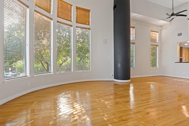 unfurnished living room with healthy amount of natural light, a ceiling fan, light wood-style flooring, and a towering ceiling