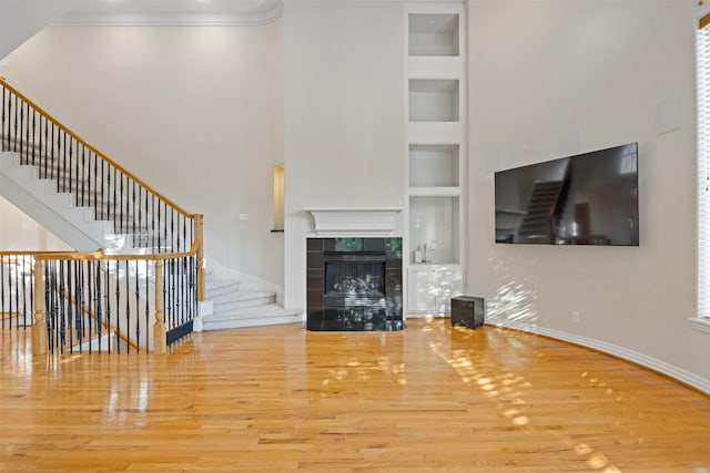 unfurnished living room featuring built in features, wood finished floors, stairs, baseboards, and ornamental molding