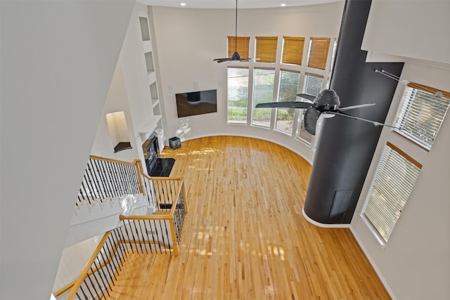 living area featuring a ceiling fan, wood finished floors, baseboards, and a towering ceiling