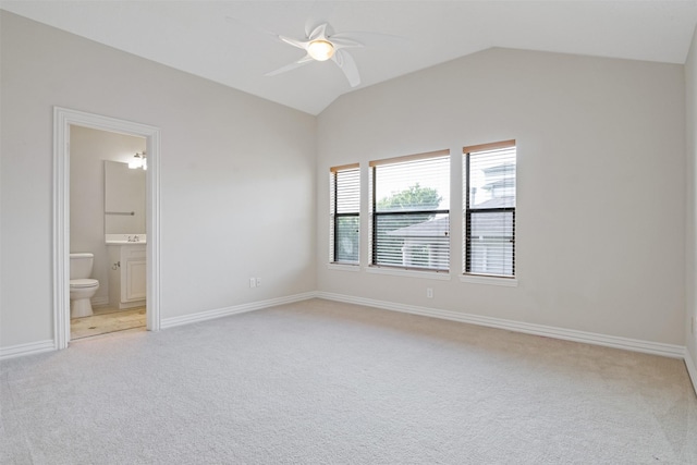 unfurnished bedroom featuring light carpet, lofted ceiling, ensuite bathroom, baseboards, and a ceiling fan