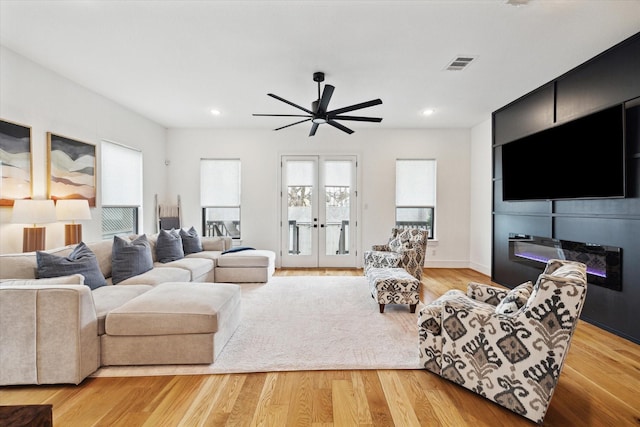 living room with a ceiling fan, recessed lighting, light wood finished floors, a glass covered fireplace, and french doors