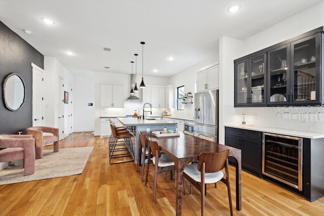 dining space featuring beverage cooler, light wood-type flooring, recessed lighting, and a dry bar