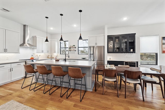 kitchen with wall chimney range hood, a sink, appliances with stainless steel finishes, a kitchen breakfast bar, and an island with sink