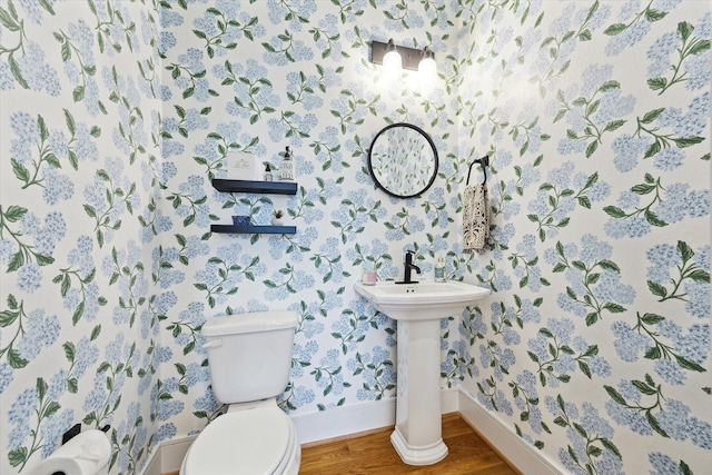 bathroom with baseboards, wallpapered walls, wood finished floors, and toilet