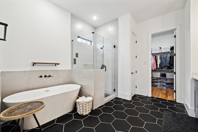 bathroom with a walk in closet, a shower stall, a freestanding bath, tile patterned flooring, and recessed lighting