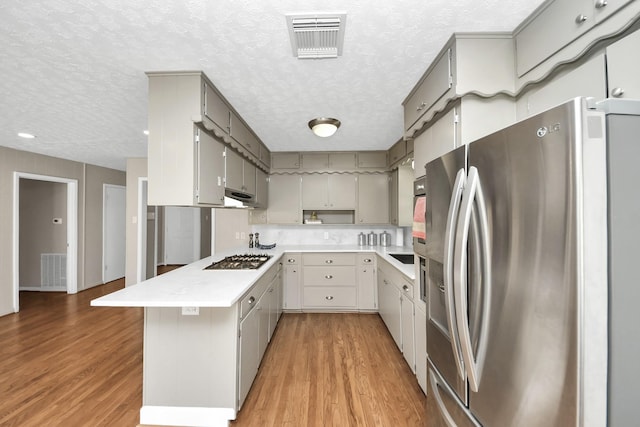 1815 Tannehill Dr, Houston, TX 77008 - kitchen with stainless steel appliances, a textured ceiling, a peninsula, light wood-type flooring, and light countertops