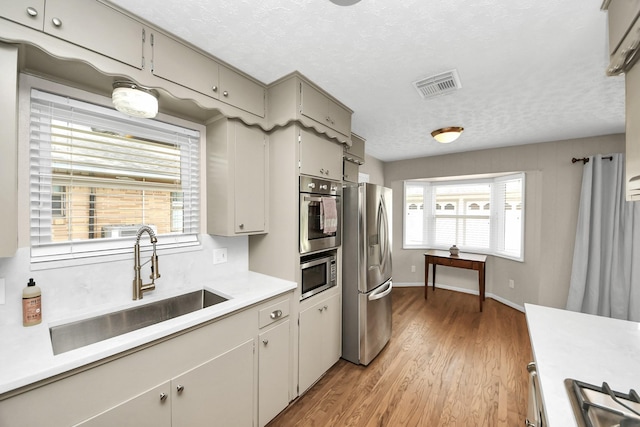 1815 Tannehill Dr, Houston, TX 77008 - kitchen featuring appliances with stainless steel finishes, a sink, light countertops, a textured ceiling, and light wood-style flooring