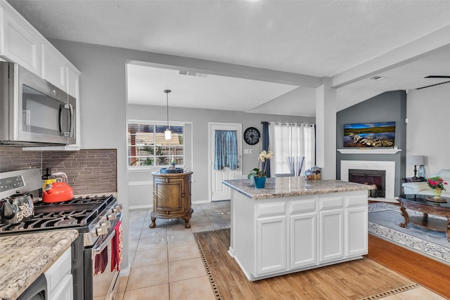 16222 Indian Cypress Dr, Cypress, TX 77429 - kitchen with appliances with stainless steel finishes, white cabinetry, a fireplace with raised hearth, decorative backsplash, and a kitchen island