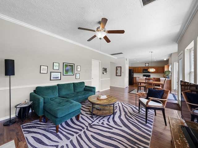 living room with dark wood-type flooring, ceiling fan, baseboards, a textured ceiling, and crown molding