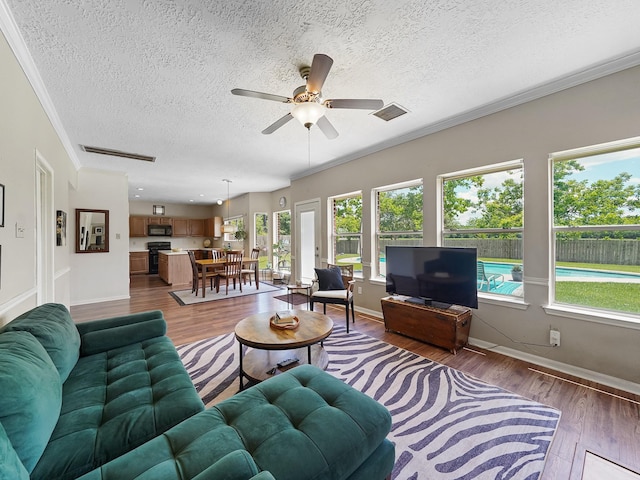 living room with ceiling fan, dark wood finished floors, a textured ceiling, ornamental molding, and baseboards