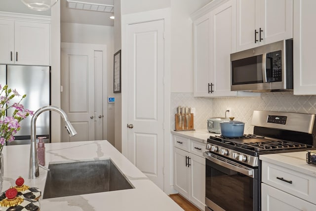 kitchen featuring appliances with stainless steel finishes, a sink, white cabinetry, tasteful backsplash, and light stone counters