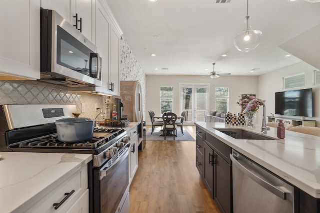 kitchen with appliances with stainless steel finishes, a sink, open floor plan, tasteful backsplash, and white cabinetry