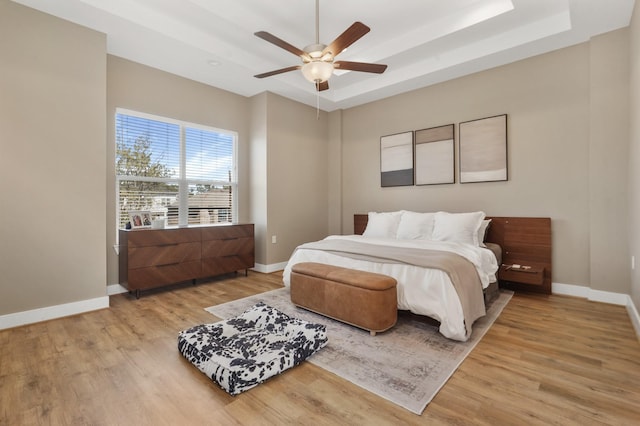 bedroom with light wood finished floors, baseboards, a raised ceiling, and ceiling fan