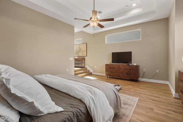 bedroom with baseboards, light wood-style flooring, a raised ceiling, and ceiling fan