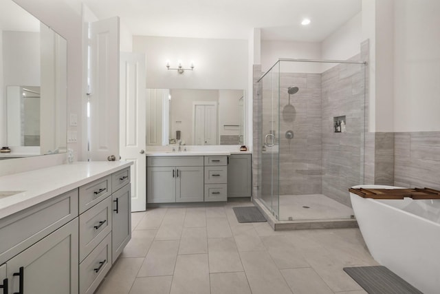 full bath featuring a stall shower, tile patterned flooring, two vanities, and a soaking tub