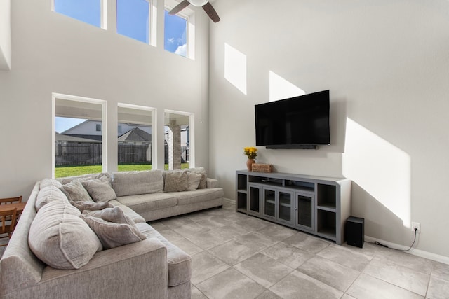 living area featuring a towering ceiling, ceiling fan, and baseboards