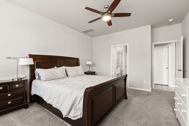 bedroom featuring light carpet, baseboards, ceiling fan, and ensuite bathroom