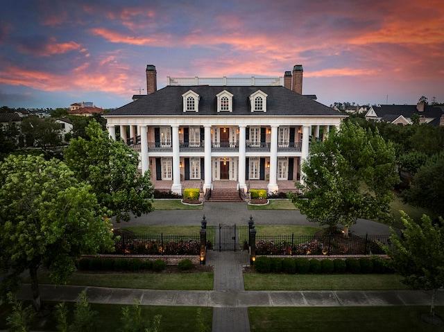 neoclassical home with a balcony, a chimney, a porch, and a gate