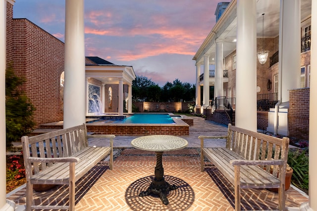 pool at dusk with a hot tub and a patio area