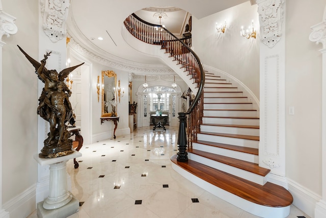 entrance foyer with stairs, a towering ceiling, arched walkways, baseboards, and a chandelier