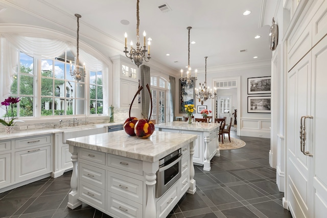 kitchen featuring a chandelier, a center island, a sink, plenty of natural light, and crown molding