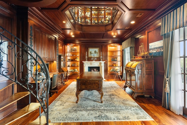 office area with crown molding, built in features, a lit fireplace, dark wood-style floors, and wood walls
