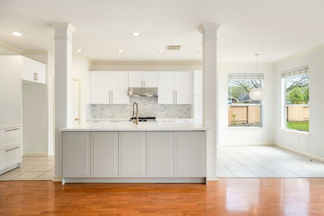 3815 Shadow Knoll Ct, Houston, TX 77082 - kitchen with decorative columns, under cabinet range hood, light countertops, crown molding, and backsplash
